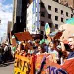 Students standing on a street in New York City holding up signs and banners to protest against the fossil fuel industry.